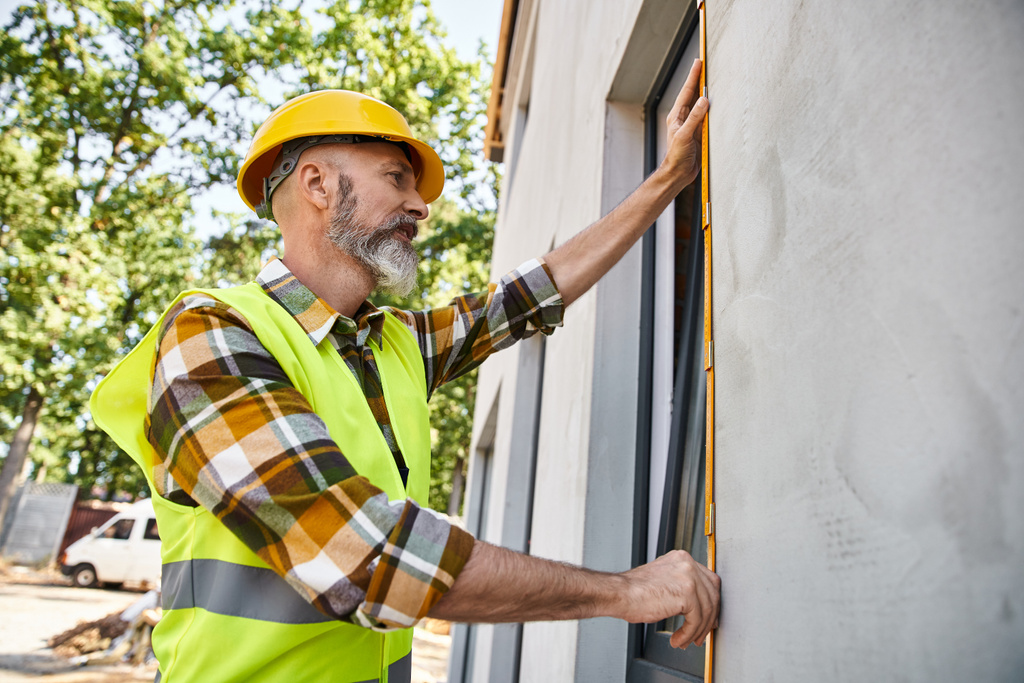 trabajador de la construcción de buen aspecto con barba ventana de medición con cinta, constructor de casa de campo - Foto, Imagen