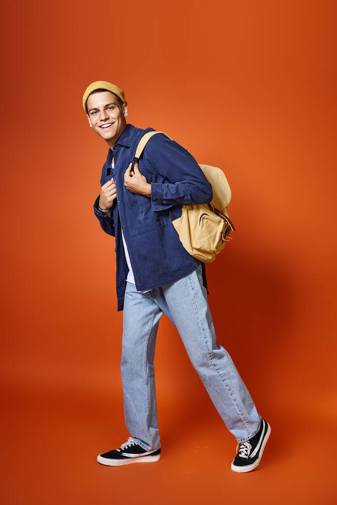 щасливий чоловік у 20-х роках з сірими очима і рюкзаком, що йде на теракотовому фоні - Фото, зображення
