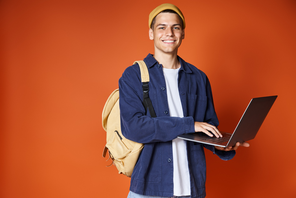 attractive student with backpack networking to laptop against terracotta background - Photo, Image