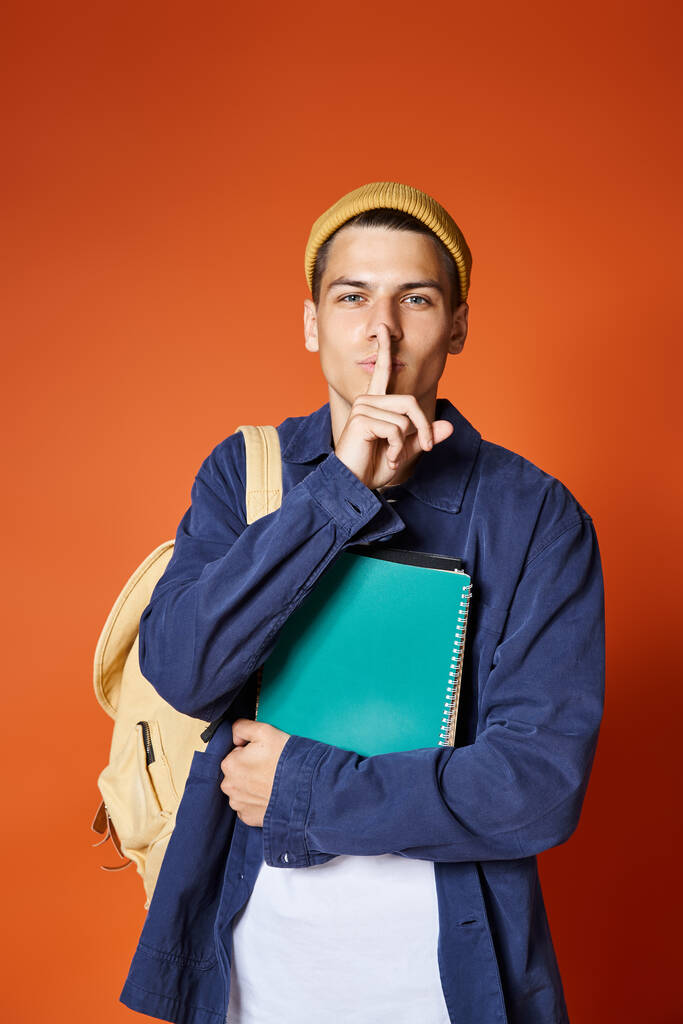 харизматичный студент 20 лет с рюкзаком и заметками, показывающими, чтобы подписать молчание на терракотовом фоне - Фото, изображение