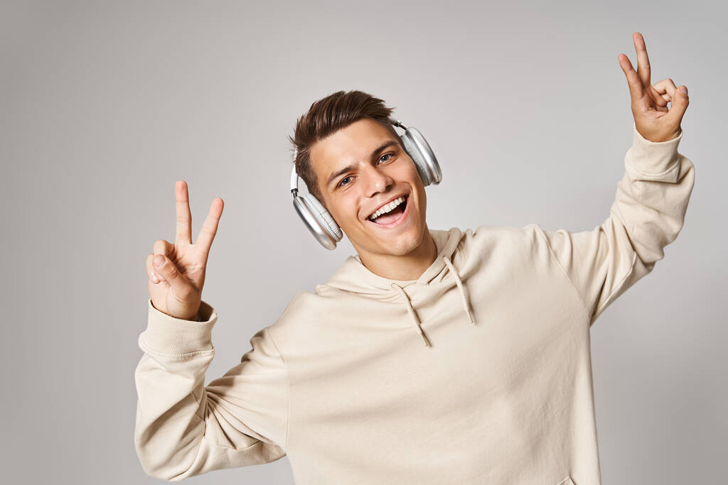 веселий студент в навушниках посміхається і показує знак спокою з руками на світлому фоні - Фото, зображення