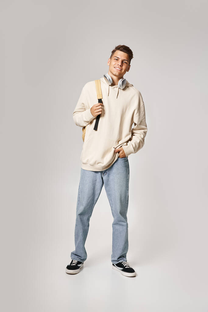 estudiante guapo en auriculares y sudadera con capucha blanca con mochila contra fondo claro - Foto, Imagen