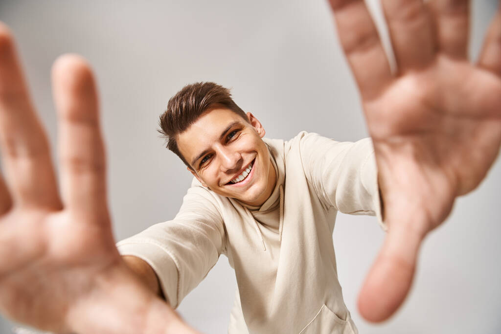 hombre alegre con el pelo castaño y los ojos grises extendiendo sus manos a la cámara sobre fondo claro - Foto, imagen