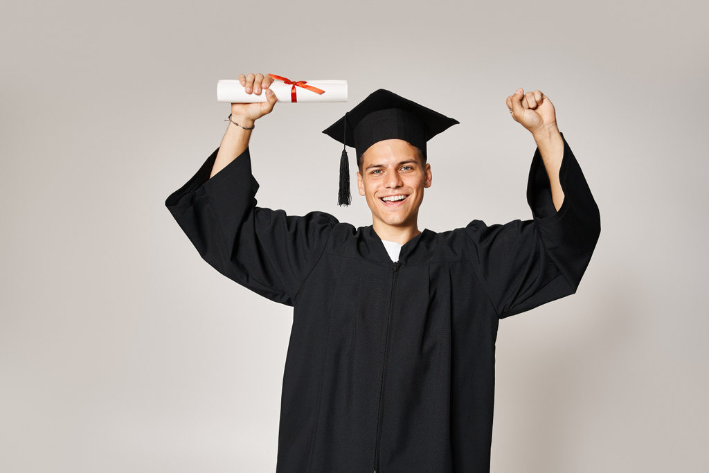 attraktive Studentin im Diplom-Outfit froh, ihr Studium auf grauem Hintergrund abgeschlossen zu haben - Foto, Bild