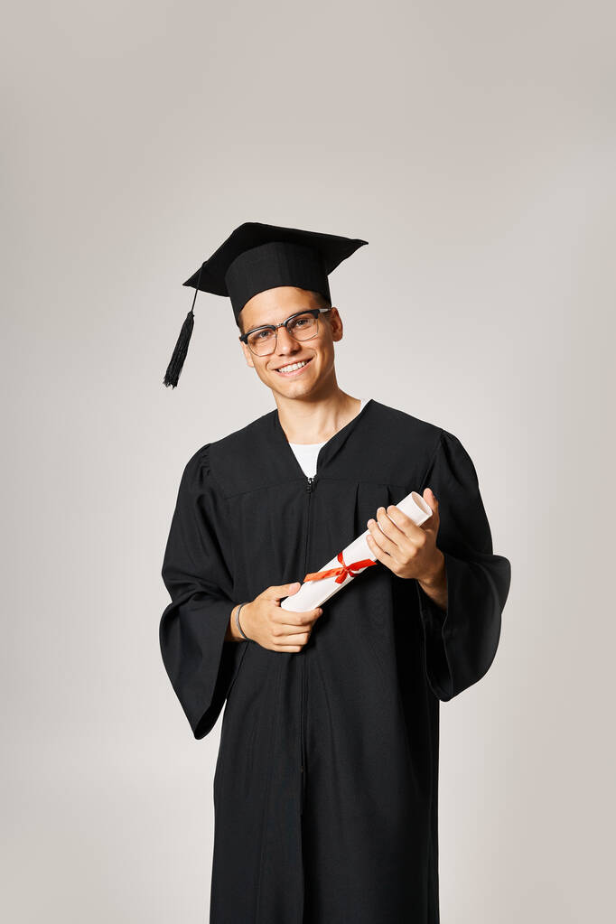 estudante confiante em roupa de pós-graduação com óculos de visão sorrindo com diploma em mãos - Foto, Imagem