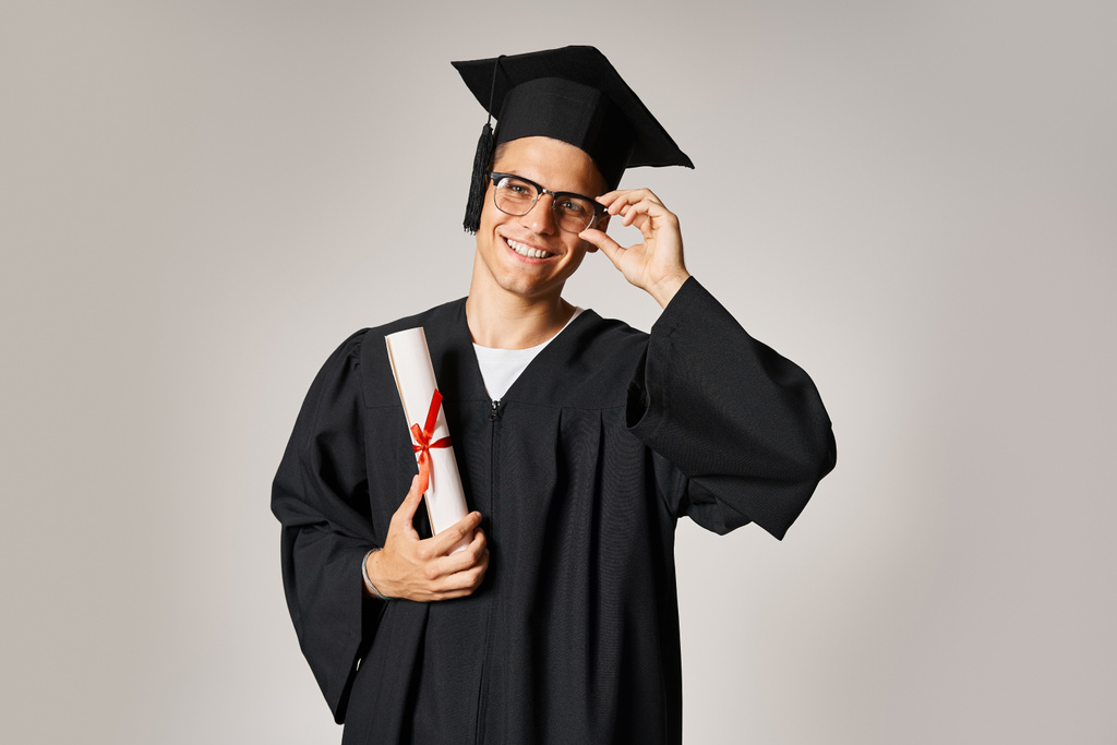 attraktive Studentin im Graduiertenkostüm, die die Hand zur Sehbrille reicht und das Diplom hält - Foto, Bild