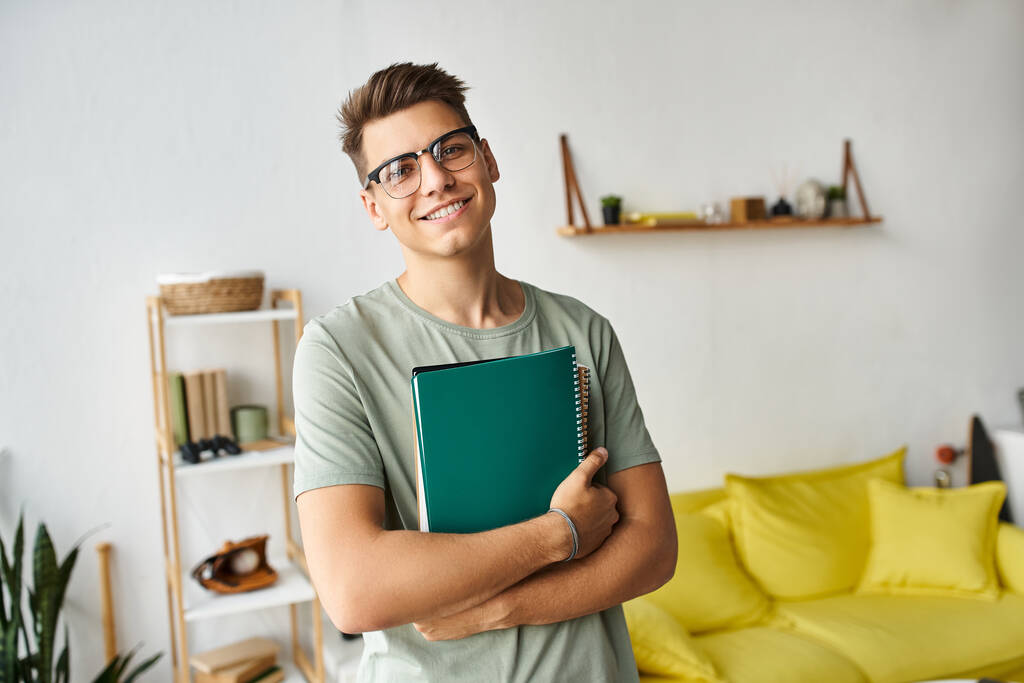 charismatický student s hnědými vlasy a brýlemi v obývacím pokoji drží poznámky s rukama - Fotografie, Obrázek