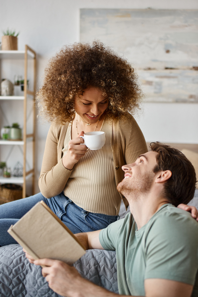 Ζεστό πρωινό διάλογο πάνω από τον καφέ, σγουρά νεαρή γυναίκα και μελαχρινή άνδρας μοιράζονται μια ζεστή στιγμή στο κρεβάτι - Φωτογραφία, εικόνα
