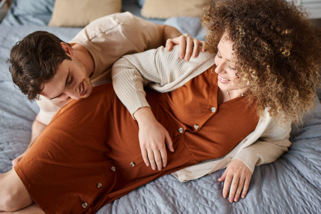 Kobieta w ciąży z mężem w sypialni, leżący w łóżku, mężczyzna rozmawiający z brzuchem żony - Zdjęcie, obraz