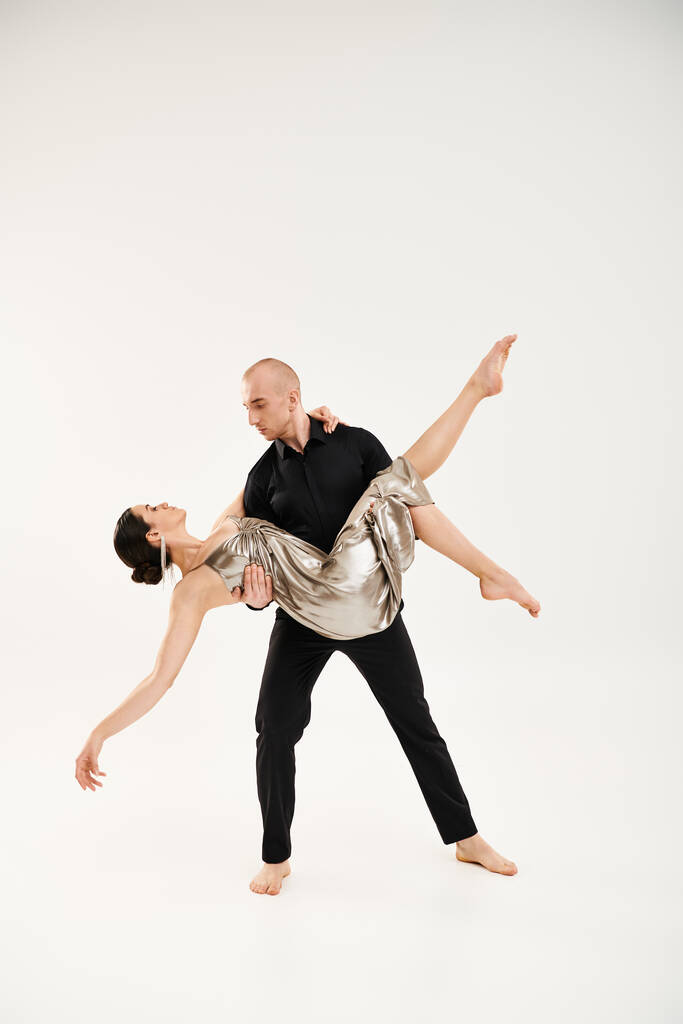 Nuori mies mustissa ja nuori nainen hopeassa kiiltävä mekko tanssia yhdessä, suorittaa akrobaattisia elementtejä studiossa vasten valkoista taustaa. - Valokuva, kuva