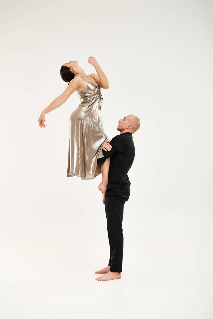 Молодой человек и женщина в серебряном платье, занимающиеся изящными танцами, демонстрирующие свои синхронные движения и акробатические навыки. - Фото, изображение