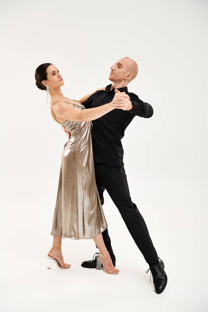 Młody mężczyzna w czerni i młoda kobieta w sukience wykonują akrobatyczne ruchy taneczne w studio. - Zdjęcie, obraz