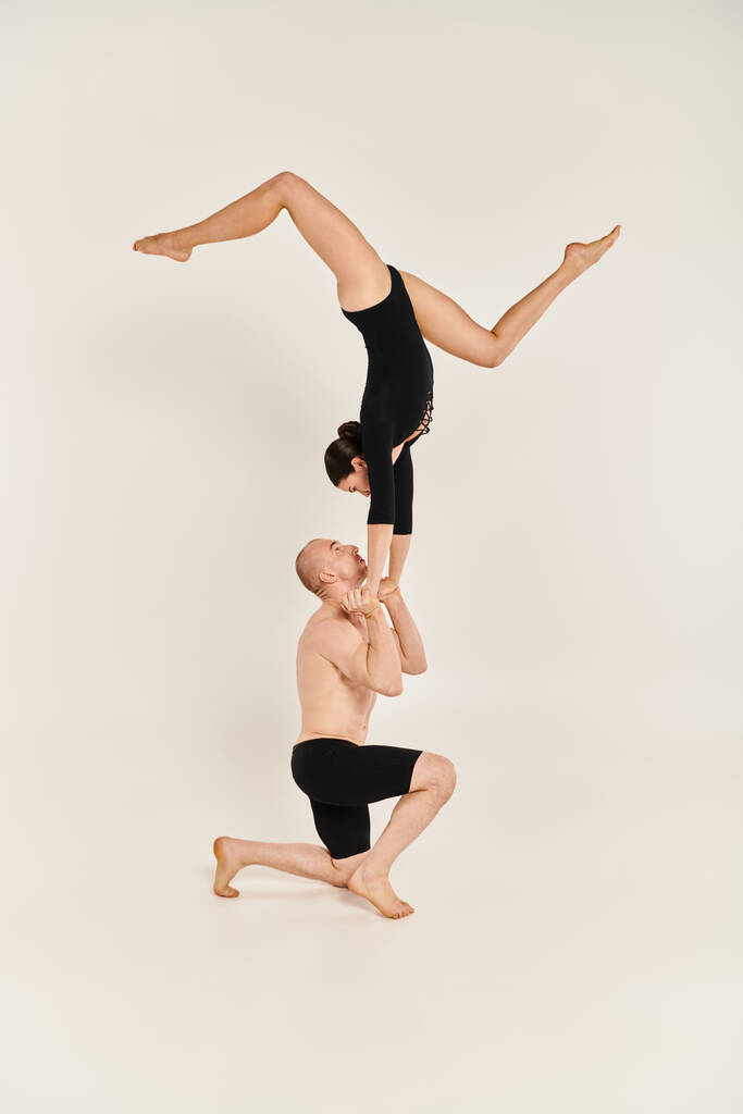 Egy fiatal, félmeztelen férfi és nő akrobatikus kézenállást végez a levegőben, tánctehetségét fehér háttér előtt mutatja be.. - Fotó, kép