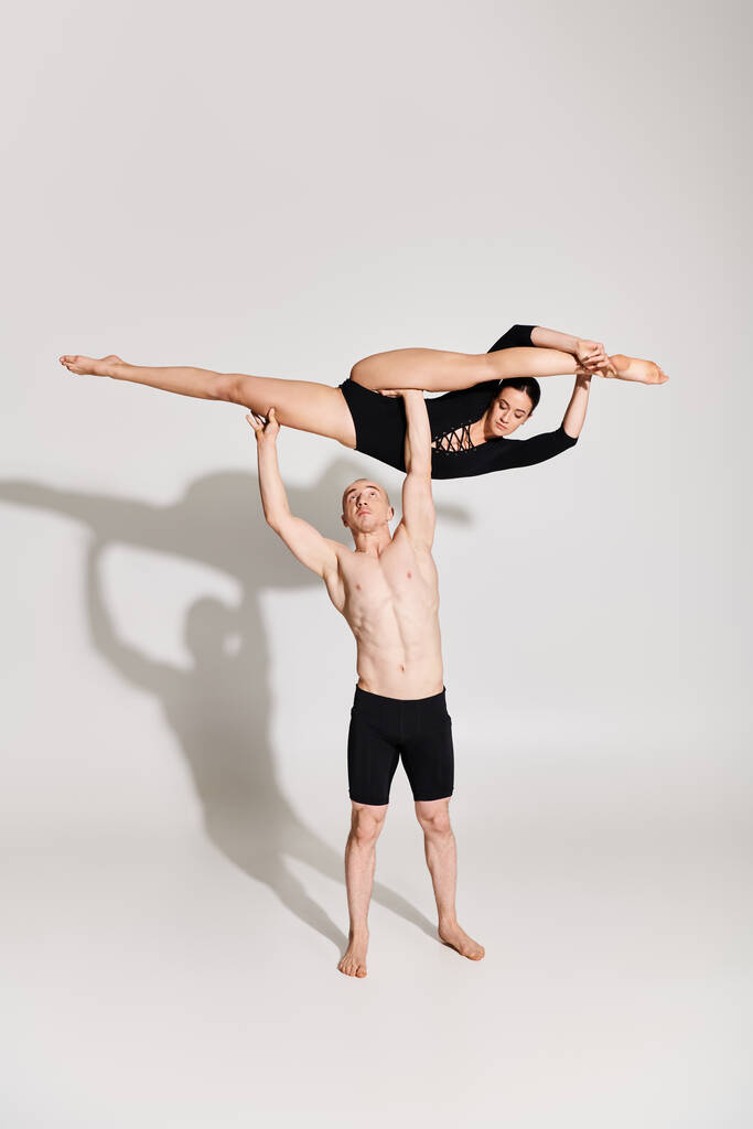 Ein hemdloser junger Mann und eine junge Frau führen einen Handstand als Teil einer akrobatischen Tanzroutine in einem Studio-Setting auf. - Foto, Bild