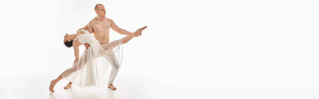 Un joven sin camisa y una mujer con un vestido blanco bailan con gracia, entrelazando y realizando movimientos acrobáticos en un entorno de estudio. - Foto, imagen