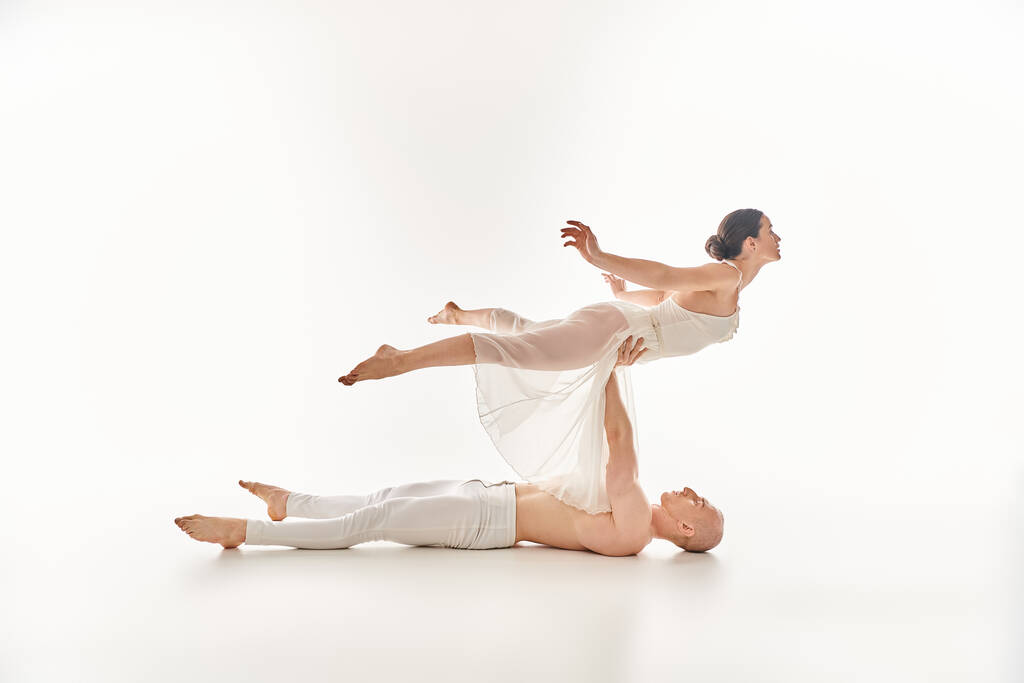 Młody mężczyzna bez koszuli i kobieta w białej sukience wykazują wdzięk i siłę, gdy wykonują układ split dance w studio.. - Zdjęcie, obraz
