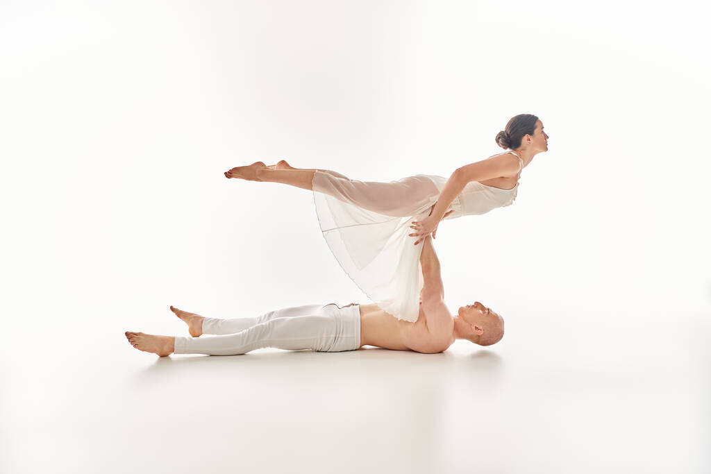 Un jeune homme torse nu et une femme en robe blanche exécutent une danse élégante et acrobatique dans un décor de studio. - Photo, image