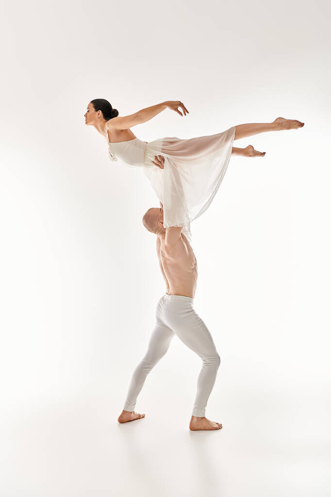 Un joven sin camisa y una mujer con un vestido blanco bailan juntos con elegancia, incorporando elementos acrobáticos, sobre un fondo de estudio blanco. - Foto, imagen