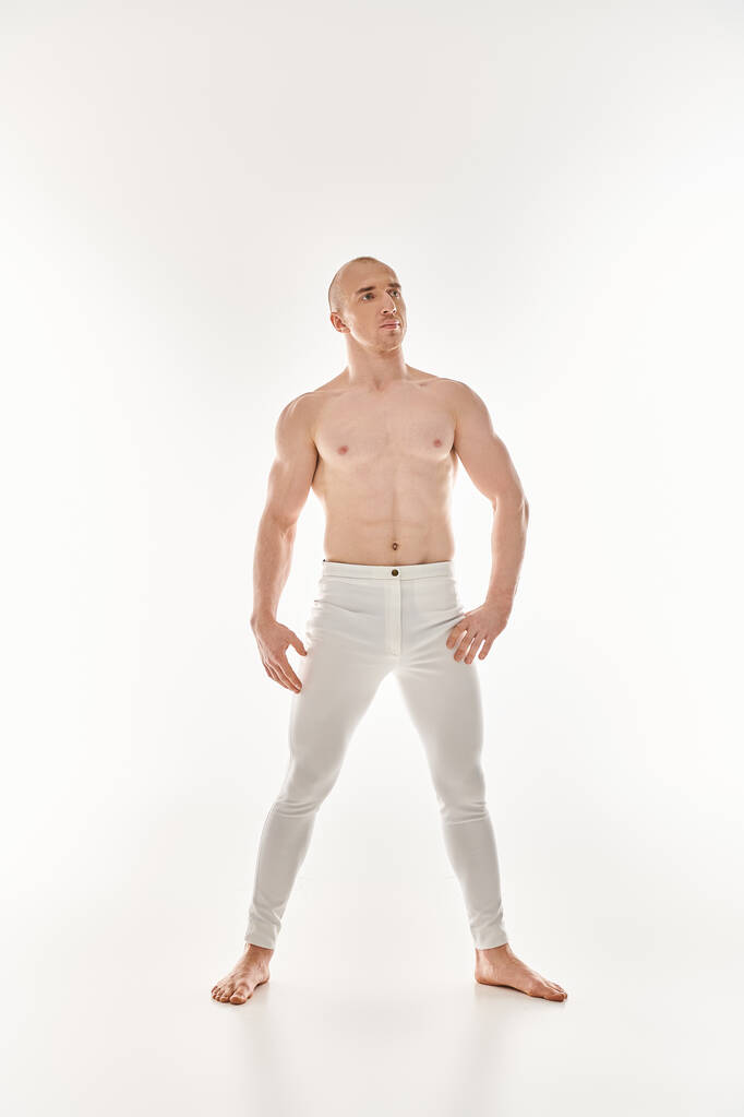 Ένας νεαρός άνδρας με λευκό παντελόνι παίρνει μια δυναμική στάση, επιδεικνύοντας ακροβατικά στοιχεία σε λευκό φόντο.. - Φωτογραφία, εικόνα