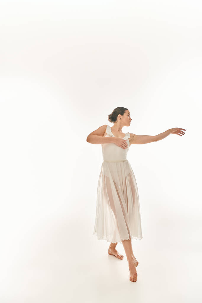 Junge Frau in elegantem weißen Kleid wirbelt vor weißem Hintergrund mit einer weißen Frisbee. - Foto, Bild