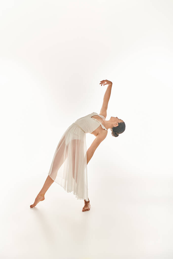 Graceful young woman in flowing white attire performs a perfect handstand in a studio setting against a clean white backdrop. - Photo, Image