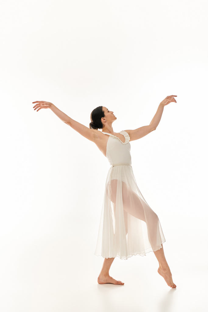 優雅な若い女性が白いスタジオの背景に対して流れる白いドレスで踊る. - 写真・画像