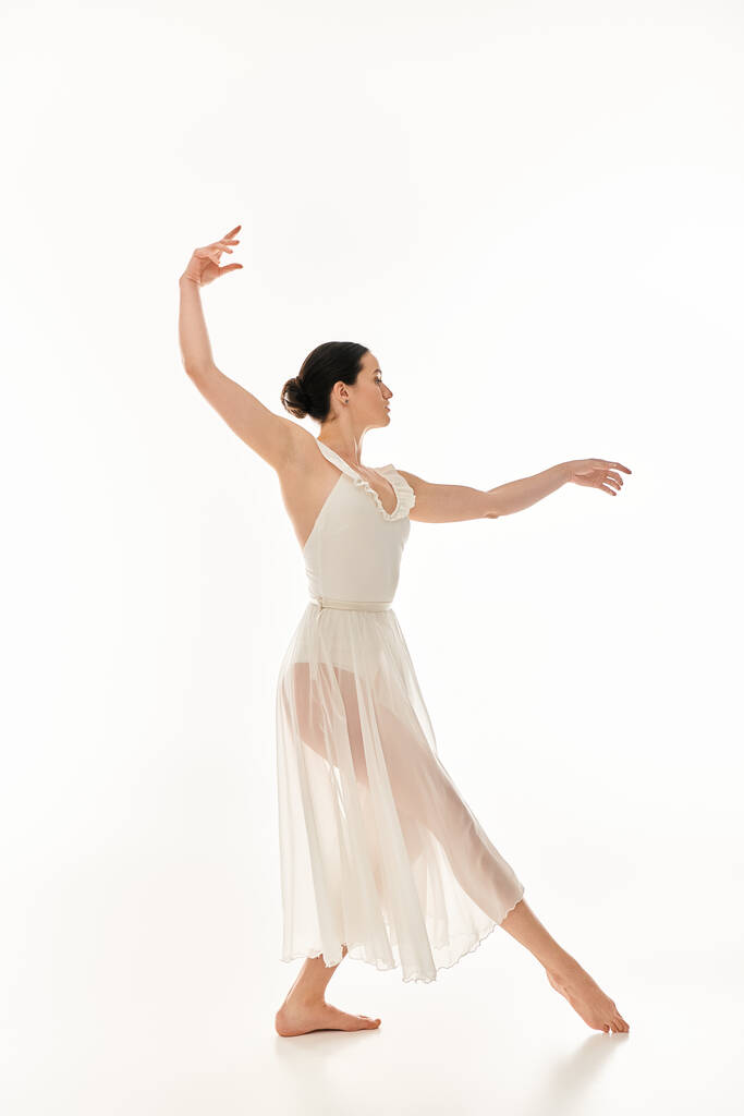 Μια χαριτωμένη νεαρή γυναίκα σε μια ροή λευκό φόρεμα εκφράζει την ομορφιά της κίνησης μέσα από το χορό. - Φωτογραφία, εικόνα