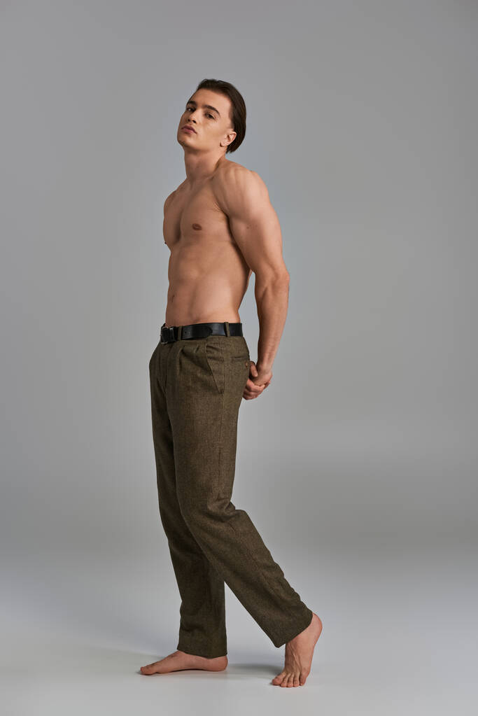 svůdné mladé bez košile mužský model v elegantních kalhotách pózuje lákavě a dívá se do kamery - Fotografie, Obrázek