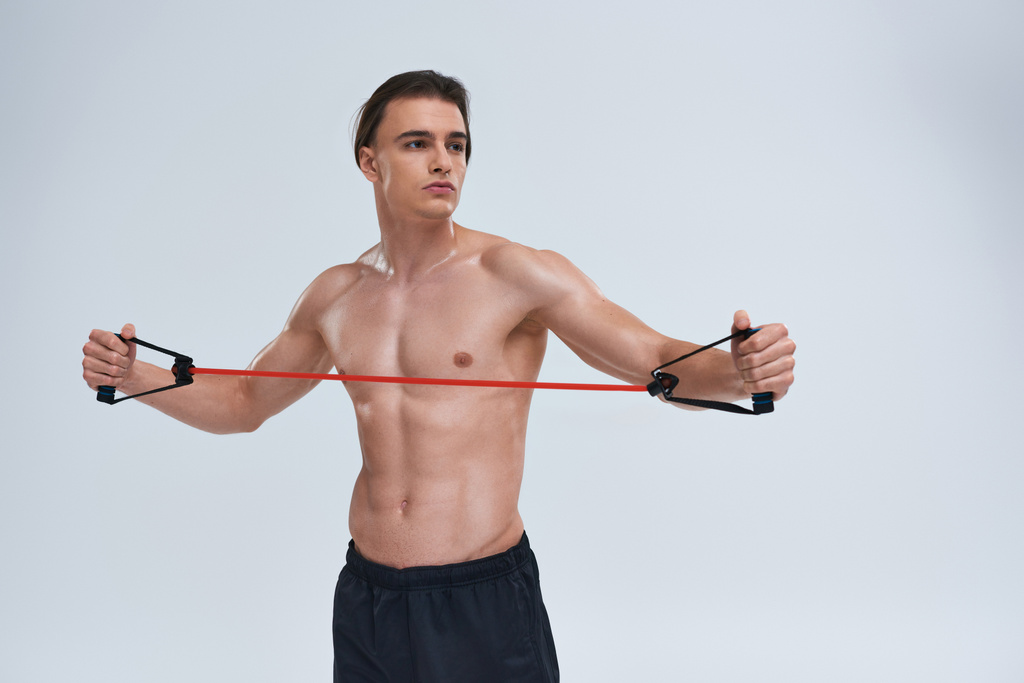 привлекательный спортивный молодой человек без рубашки в черных штанах тренируется с фитнес-экспандером и смотрит в сторону - Фото, изображение