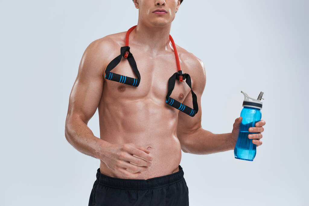 cropped view of sexy athletic man in black pants posing topless with bottle and fitness expander - Photo, Image