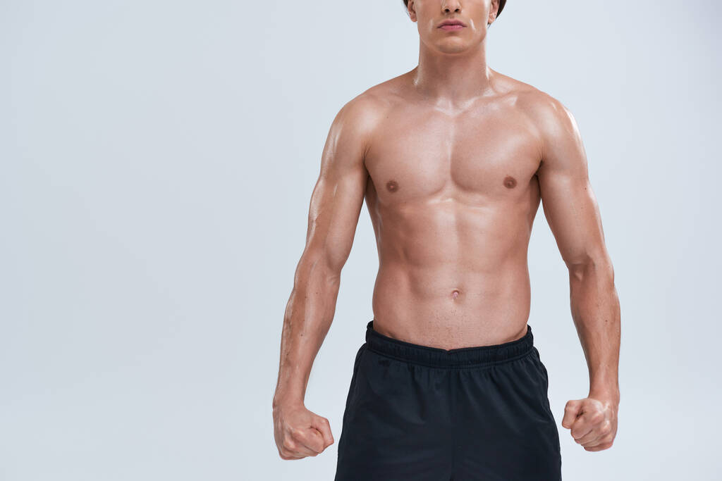 vista ritagliata di seducente giovane atletico uomo in pantaloni neri in posa topless su sfondo grigio - Foto, immagini