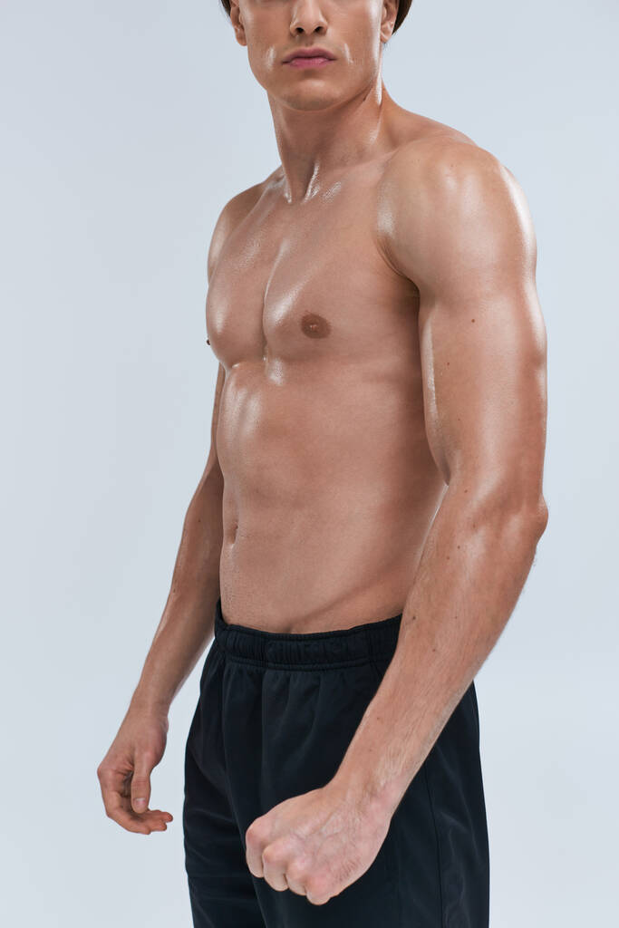 Ausgeschnittene Ansicht des verlockenden jungen athletischen Mannes in schwarzer Hose, der oben ohne auf grauem Hintergrund posiert - Foto, Bild