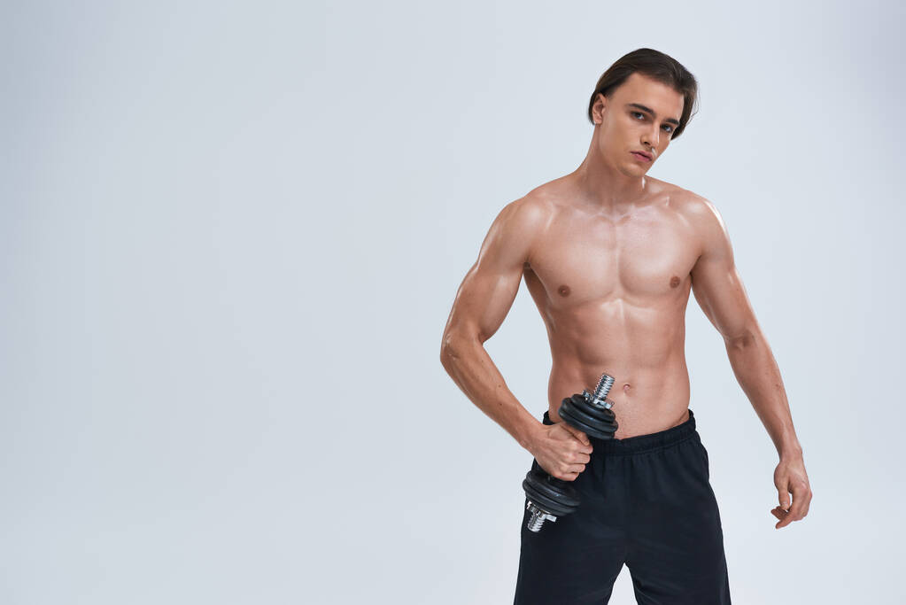 atractivo atlético hombre posando en topless ejercicio activamente con la mancuerna y mirando a la cámara - Foto, imagen