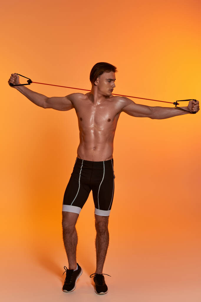 vonzó fiatal sportos férfi fekete rövidnadrágban pózol félmeztelen és gyakorló fitness expander - Fotó, kép