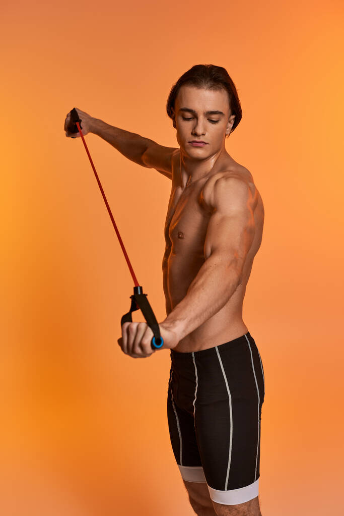 atrakcyjny młody sportowy mężczyzna w czarnych spodenkach pozowanie topless i ćwiczenia z ekspanderem fitness - Zdjęcie, obraz