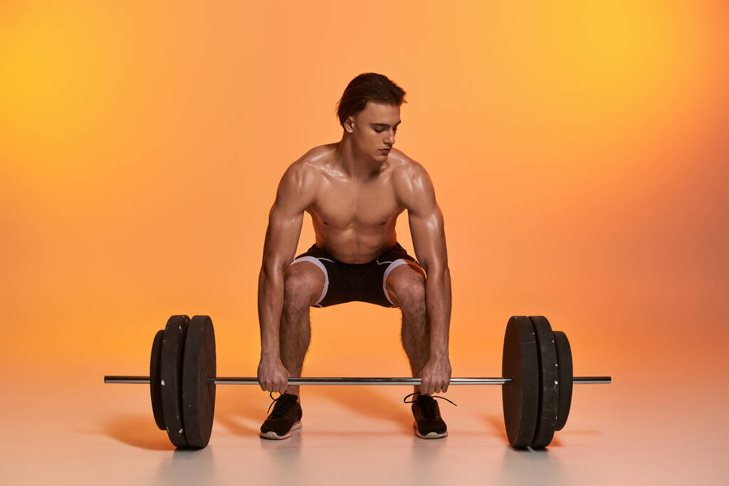 alluring shirtless muscular man in black pants exercising with barbell on vibrant orange backdrop - Photo, Image