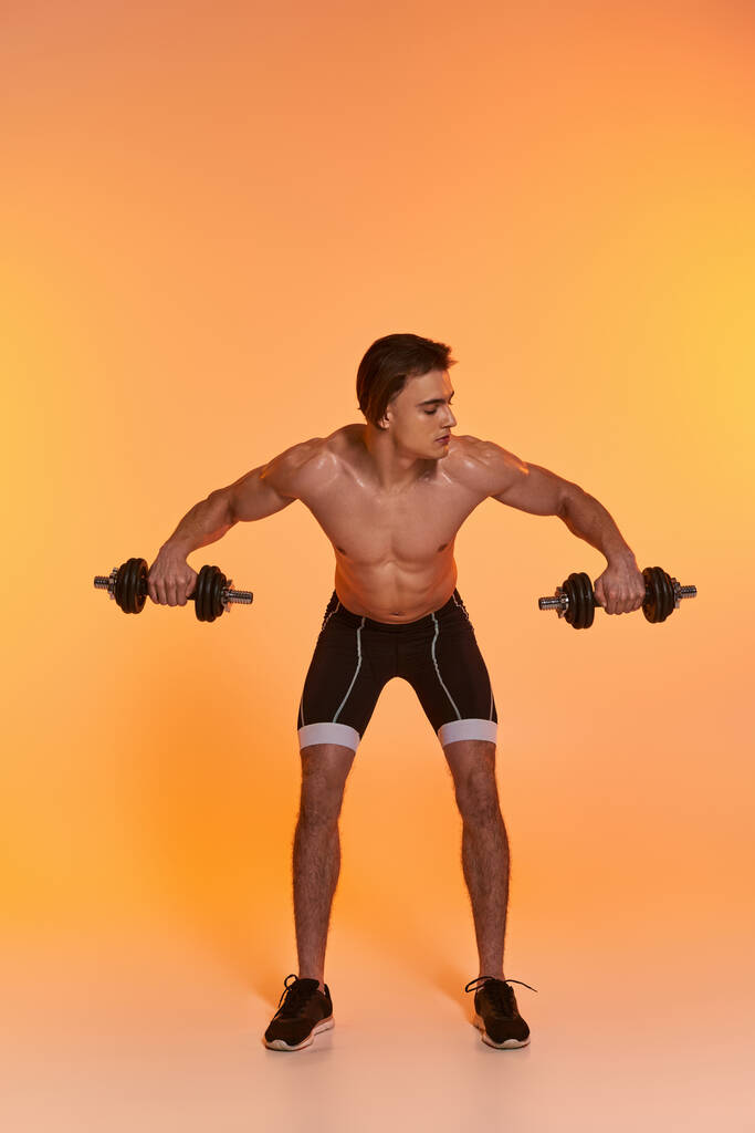 atrakcyjny muskularny mężczyzna bez koszuli w czarnych spodenkach sportowych trening z hantlami na żywym tle - Zdjęcie, obraz