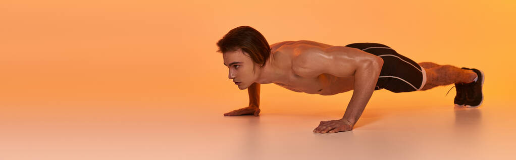 młody mężczyzna bez koszuli w czarnych spodenkach ćwiczy aktywnie i odwraca wzrok na pomarańczowym tle, baner - Zdjęcie, obraz