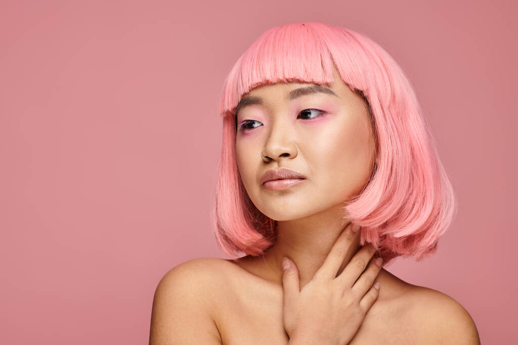 séduisante femme asiatique avec les cheveux roses regardant vers le côté et touchant son cou sur fond vibrant - Photo, image