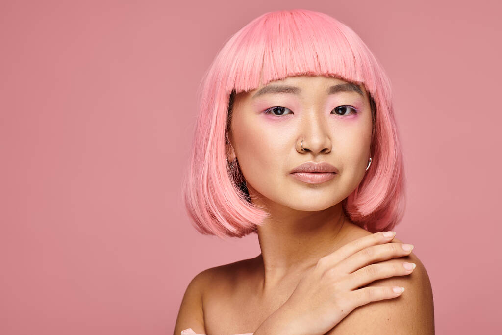 όμορφη γυναίκα 20 ετών με ροζ μαλλιά και μύτη σκουλαρίκια αγγίζοντας τον ώμο σε ζωντανό φόντο - Φωτογραφία, εικόνα