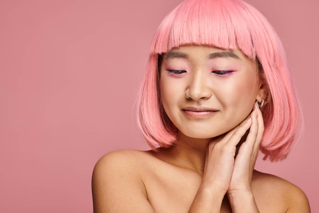красива азіатська жінка з рожевим волоссям і макіяжем дивиться вниз руками на яскравому фоні - Фото, зображення