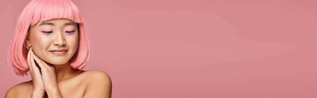горизонтальный снимок милой азиатской женщины с розовыми волосами, смотрящей вниз с руками на ярком фоне - Фото, изображение