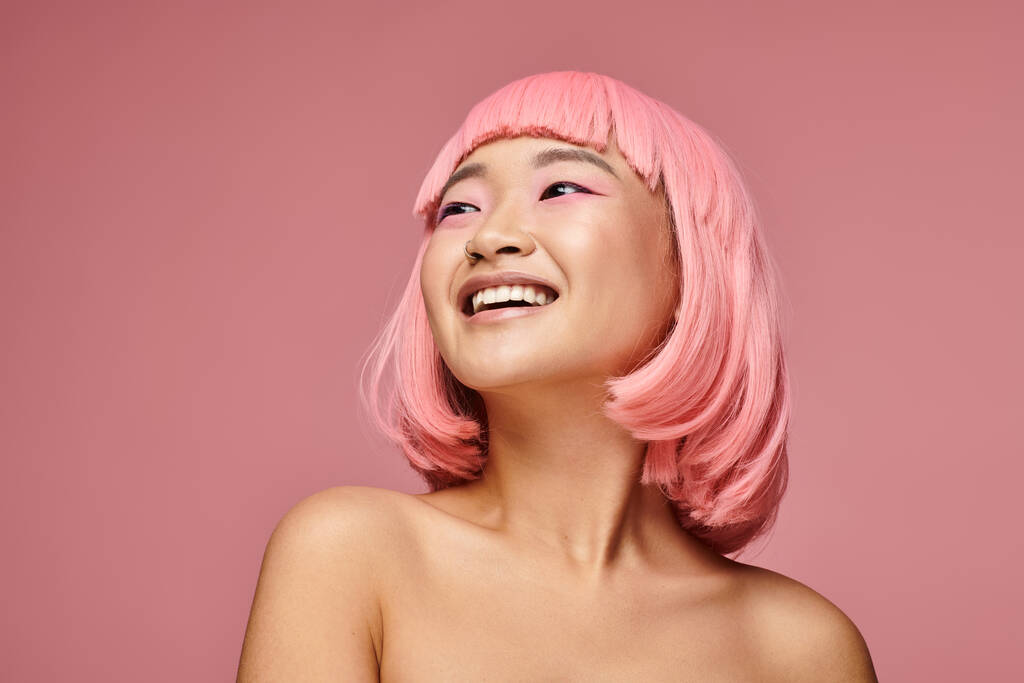 портрет чарівної азіатської дівчини з пірсингом носа сміється, дивлячись вгору на яскравий фон - Фото, зображення