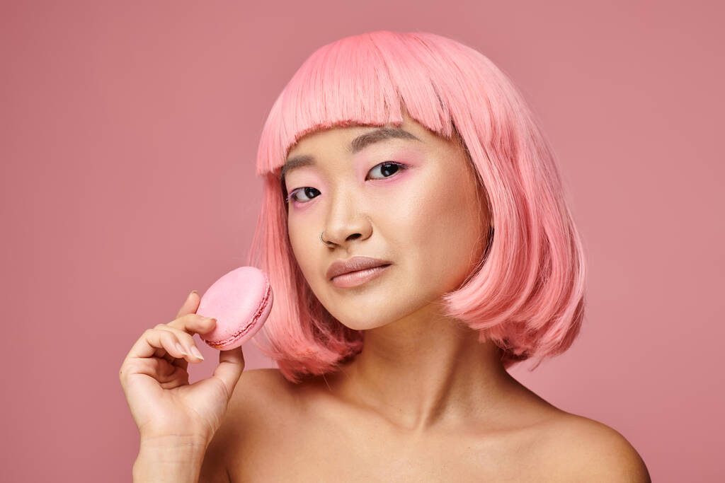 hermosa asiático joven mujer con rosa pelo posando con macaroon en vibrante fondo - Foto, Imagen