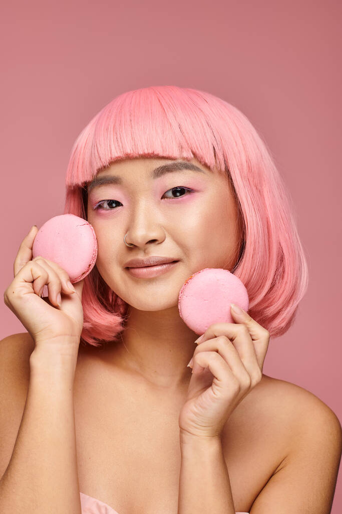 piękny Azji młoda kobieta z różowe włosy i makijaż gospodarstwa makaroniki z ręki w żywe tło - Zdjęcie, obraz