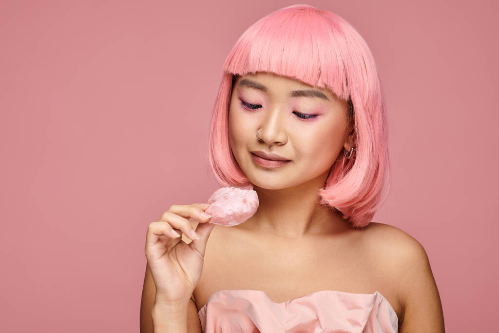 bonito asiático mulher no ela 20s com rosa cabelo e maquiagem olhando para mochi contra vibrante fundo - Foto, Imagem