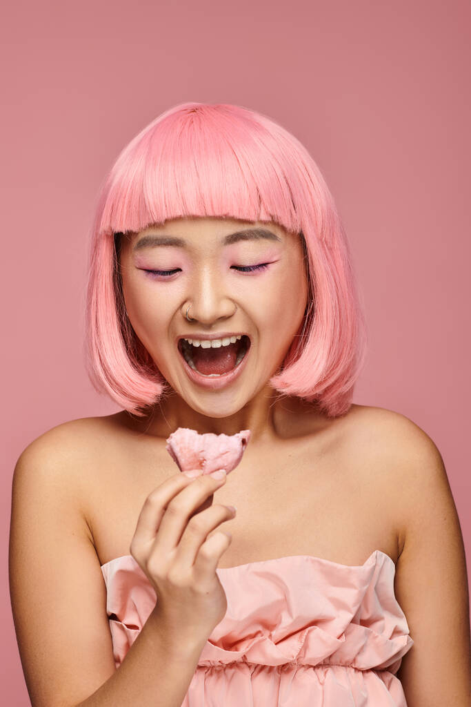 όμορφη ασιατική νεαρή γυναίκα με ροζ μαλλιά έκπληκτος από mochi σε ζωντανή φόντο - Φωτογραφία, εικόνα