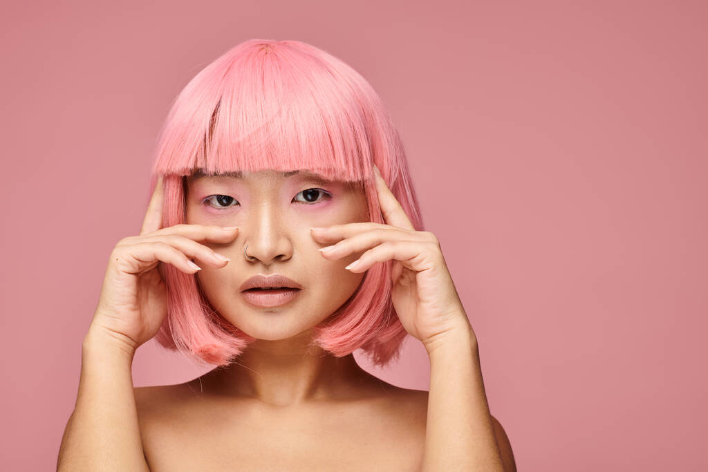 attraktive asiatische junge Frau mit rosa Haaren und Make-up posiert mit den Händen vor lebendigem Hintergrund - Foto, Bild