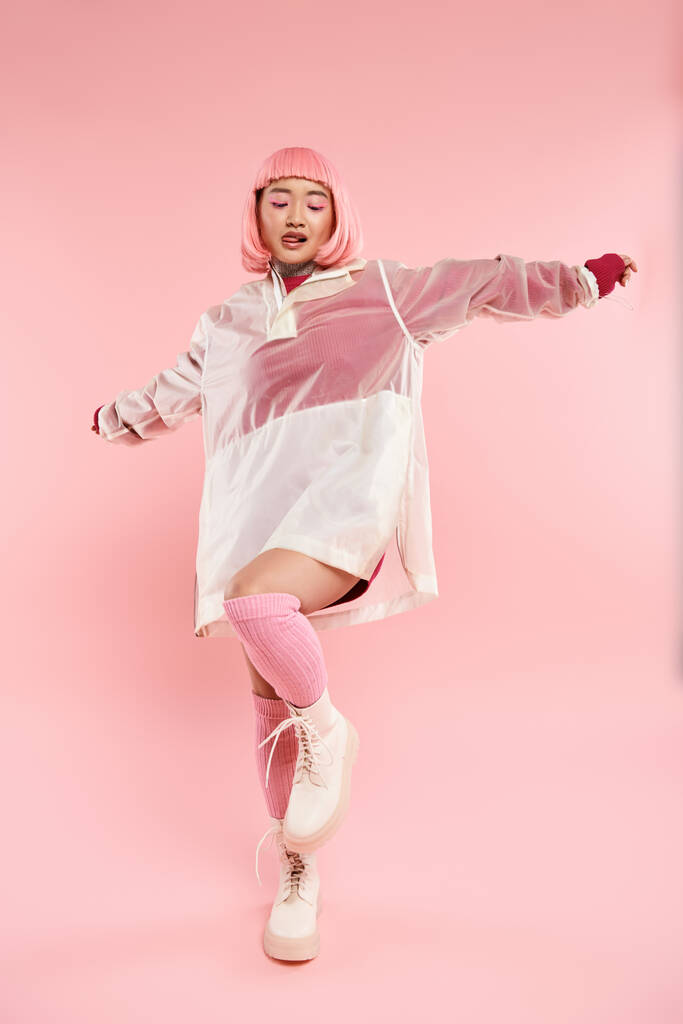 aantrekkelijke aziatische vrouw in de 20 met roze haar in stijlvolle outfit poseren tegen levendige achtergrond - Foto, afbeelding