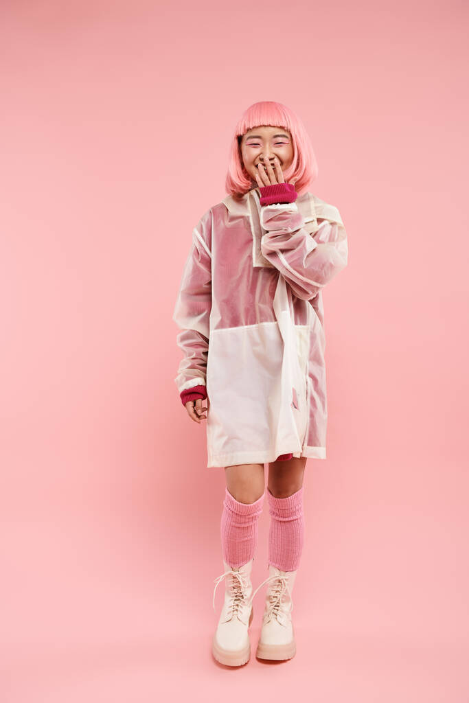 Ευτυχισμένη Ασιάτισσα στα 20 της με ροζ μαλλιά σε στυλάτο ντύσιμο γελώντας σε ζωντανό φόντο - Φωτογραφία, εικόνα